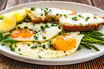 Crispy toasted bread with cheese, green asparagus and fried eggs with runny yolks on wooden table	