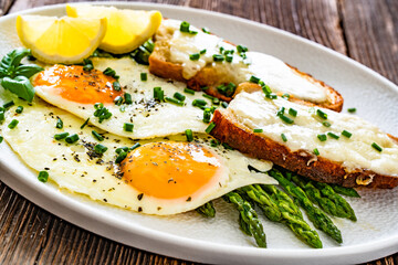 Crispy toasted bread with cheese, green asparagus and fried eggs with runny yolks on wooden table	