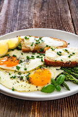 Crispy toasted bread with cheese, green asparagus and fried eggs with runny yolks on wooden table	