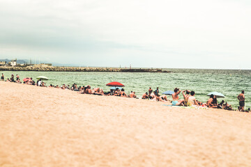 People enjoy a sunny day at the beach, relaxing and sunbathing along the coast. A vibrant beach scene with people sunbathing, relaxing under umbrellas, and enjoying the seaside during a sunny day.
