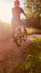 Woman riding cruiser bike riding in remote area on sunset. Back view. Cyclist girl biker enjoys freedom, healthy lifestyle, sport activity. Active summer holidays.
