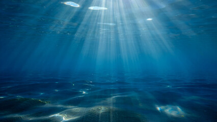 Sunlight streams through the clear blue ocean water creating beautiful patterns on the sandy seabed below