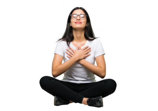 A young woman with glasses and long black hair sits in a meditative pose with her eyes closed and hands on her chest isolated on transparent background