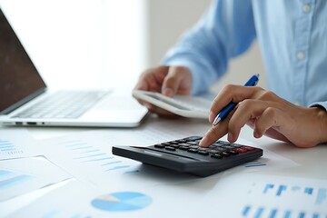 Close up of a person s hands using a calculator and pen while working with financial reports and a laptop computer in a bright office setting