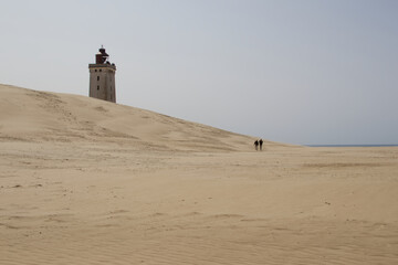People Walking Towards Lighthouse on Vast Sand Dunes