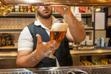 Bartender pouring beer from tap in restaurant pub, filling glass with fresh cold beverage