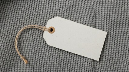 Close-up of a blank white clothing tag with a string, resting on a textured gray knit fabric. Ready for your design or text.