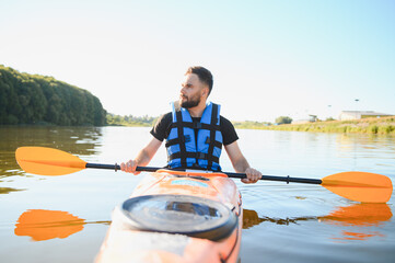 Kayaker paddling kayak on river in sunny day wearing life vest