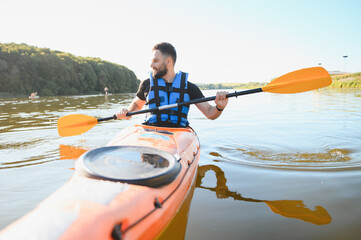 Kayaker paddling orange kayak on calm lake or river, enjoying water sports