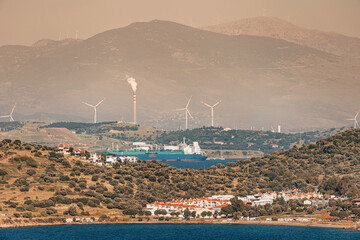 Cargo ship sailing near wind turbines and a smoking chimney, highlighting the conflict between...