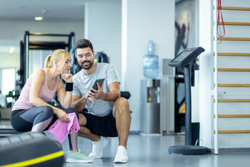 Mid adult woman and personal fitness trainer having conversation during workout break at gym.