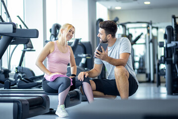Mid adult woman and personal fitness trainer having conversation during workout break at gym.