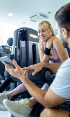 Mid adult woman and personal fitness trainer having conversation during workout at gym.