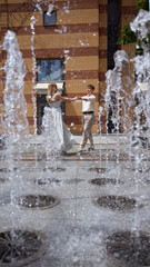 Couple dances joyfully amid water fountain sprays in a lively urban plaza setting. Concept of urban romance and spontaneity.