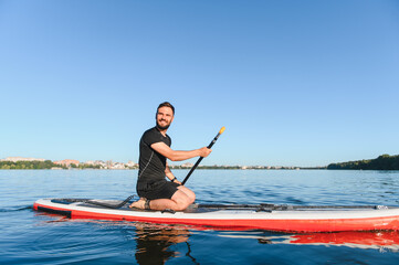 Sportsman kneeling on sup board paddling on lake in summer