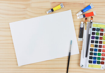 flat lay of artist workspace. Blank paper, Drawing tools, stationary supplies, Watercolor paints and brushes and paper on wooden table.