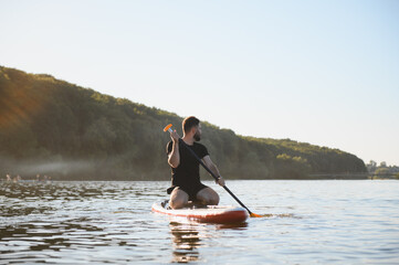 Sportsman kneeling on sup board paddling on river at sunset