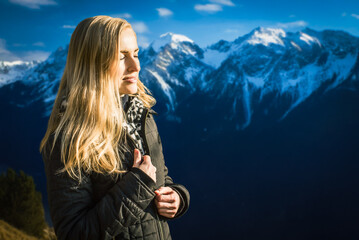 Happy young woman breathing fresh air in mountains. Woman with long blonde hair in jacket standing...