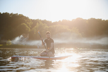 Man enjoying stand up paddleboarding on sunny lake