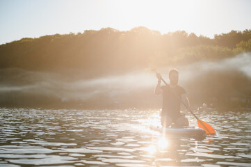 Sportsman kneeling on sup board paddling on lake at sunset
