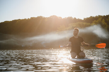Man kneeling on sup board paddling on lake at sunset
