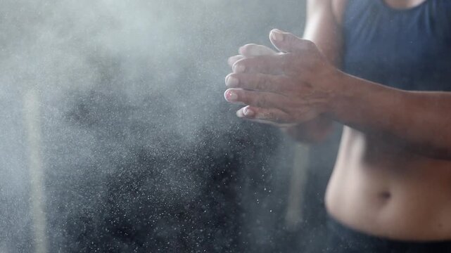 Fitness woman in gym applies chalk to her hands, with big dust cloud