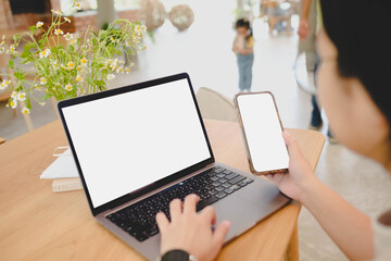 A parent working on a laptop and phone, both with blank screens, in a family-friendly cafe with a child in the background. A work-life balance mockup.