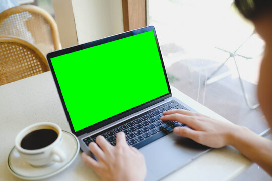 A person working on a laptop with a blank green screen in a cafe by the window. A versatile chroma key mockup for website or video content.