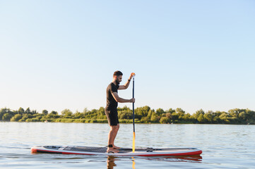 Sportsman paddling on sup board on lake at sunset