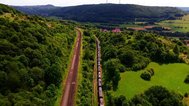 Freight Train Traveling Through Lush Green Valley Beside Parallel Railway Tracks in Scenic Countryside Landscape