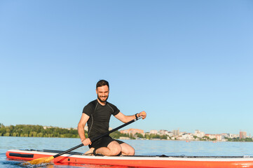 Sportsman kneeling on sup board paddling on lake during summer day