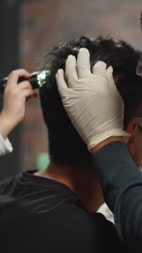 African-American biologist examines man hair and head skin while little girl use scanner in laboratory close backside view