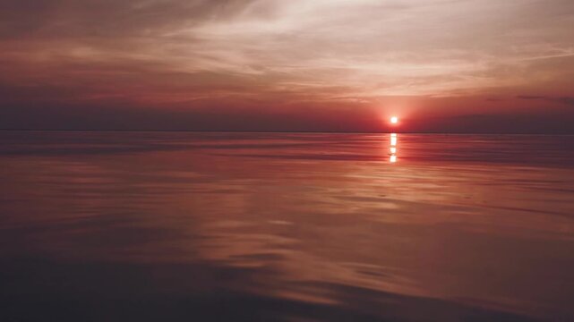 A peaceful sunset over the calm sea. Vibrant orange and blue gradient sky reflects on still water. Minimalist seascape filmed at twilight, ideal for background or meditative footage.