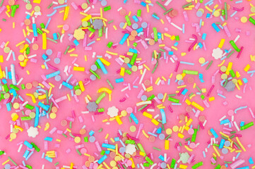 Pink icing with scattered unicorn confetti shapes sugar cake decoration background texture