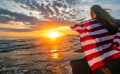 Young woman holding national American flag walking ocean beach. America Independence Day concept