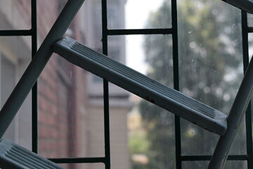 Detail of an outdoor ladder against a metal grid with sunlight filtering through on a bright day