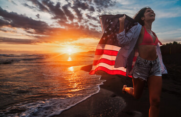 Happy woman holding american USA flag and running on the beach. Independence Day, travel concept
