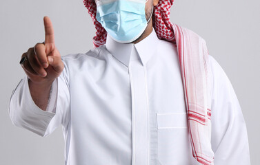 saudi arabian man in thob standing wearing face mask front facing showing index finger