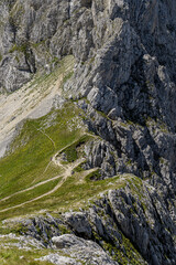 High-altitude view of mountain trail winding through rugged cliffs with small hikers visible. Dramatic alpine landscape ideal for trekking, adventure sports, exploration, and nature photography.
