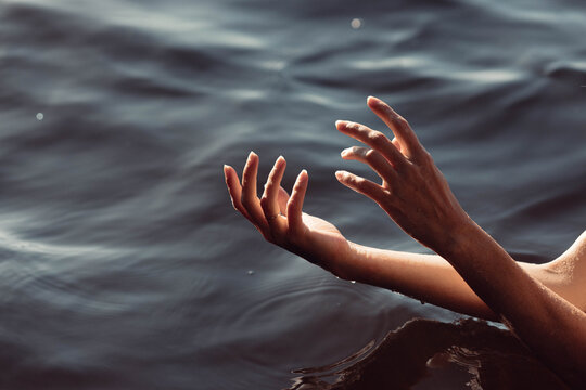 Soft hands emerge from calm water, fingertips barely breaking the surface as they reach out. gentle light reflects on the rippling waves, creating a peaceful atmosphere at twilight