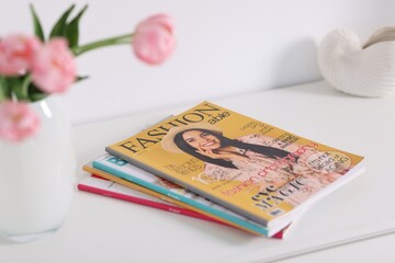 Many different trendy magazines and tulip flowers on white cabinet indoors, closeup