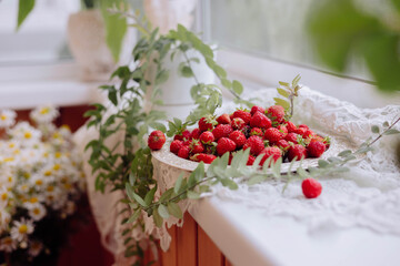 A vibrant collection of fresh strawberries rests on a decorative plate surrounded by lush greenery, creating a lively atmosphere on a sunlit windowsill filled with charm