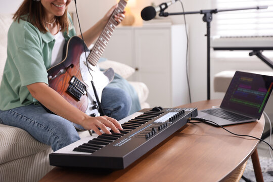 Smiling woman working with MIDI keyboard and guitar at table in home studio, selective focus
