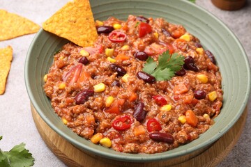 Tasty chili con carne in bowl and nachos on grey table, closeup