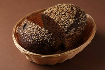 Fresh rye bread with seeds in wicker basket on brown background, closeup