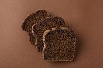 Pieces of fresh rye bread on brown background, top view