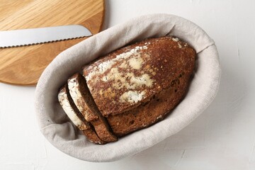 Fresh rye bread in basket on white textured table, flat lay