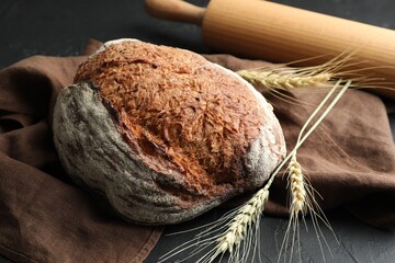 Loaf of fresh bread, rolling pin and spikes on black table, closeup