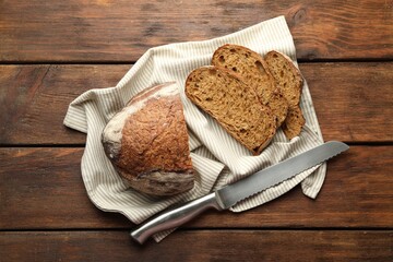 Pieces of fresh bread and knife on wooden table, flat lay