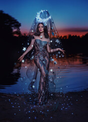 Fantasy woman queen of night lady moon, crown glows on head, black dress cape shining stars fairy girl goddess creative costume beauty face. Summer dark nature water lake river sky sunset art portrait